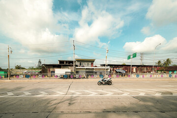 Scenic view of a busy road with a motorcycle passing by under a partly cloudy sky, capturing a moment of movement and daily life