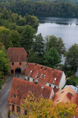 Naklejka premium A high-angle view shows old tiled-roof houses by the lake surrounded by autumn trees. Concept of historic charm, travel inspiration, seasonal landscape and scenic architecture.