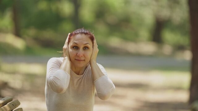 Stressed woman covering ears in park