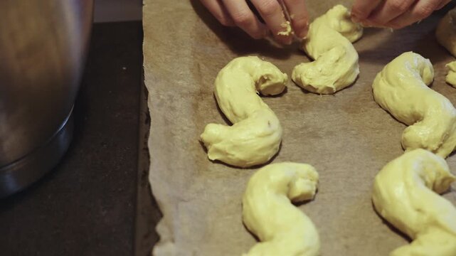 Hands of female baker working and placing dough of s-shaped yellow pastries, traditional Scandinavian holiday bakery desaturated footage easily color matched