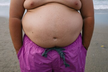 Caucasian adult male with large belly in pink swim trunks at beach