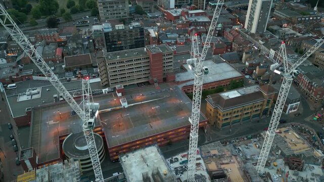 An aerial view of a cityscape featuring multiple large white construction cranes amidst buildings and streets.