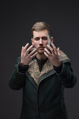 A young man in a warm coat with a high collar covering half of his face, melancholic and depressive cyberpunk style, the fashion of the gloomy future. Posing in the studio on a grey background