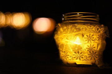 Glowing candle jar with lace decor and warm bokeh lights at night