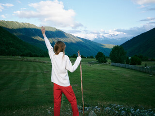 Naklejka premium Outdoor scene of a woman standing in a green valley, mountains in the distance, arms raised in triumph, conveying freedom, exploration and joy in vast natural scenery.