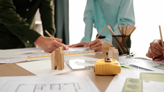Smart architect and safety engineer discussion about building blueprint on table with architectural document, measurement tools and wooden block scatter around at modern office. Closeup. Delineation.