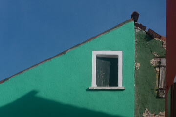 Dettaglio del tetto di una casa dipinta di verde di Burano con una finestra dalla cornice bianca