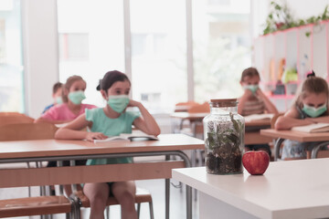 Multiracial group of kids wearing face masks working at class, writing and listening explanations...