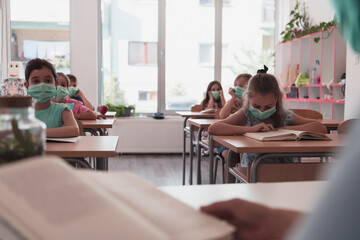 Multiracial group of kids wearing face masks working at class, writing and listening explanations of teacher in classroom