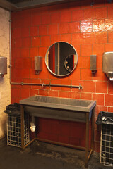 Industrial-Style Bathroom Features a Metal Sink, Circular Mirror, and Bright Red Tile Wall in a Modern Urban Setting