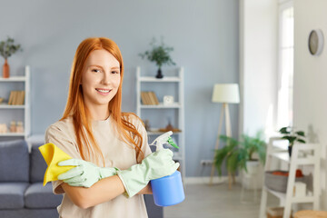 Portrait of a smiling woman holding a cleaning cloth and spray while dusting at home. She engages in household chores, showing focus on housecleaning and keeping home clean and tidy.