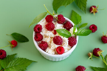 Cottage cheese with raspberries and green leaves on a green background