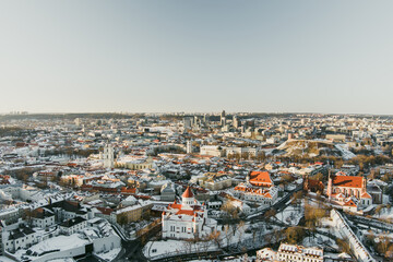 Obraz premium Drone view of snow-covered Vilnius Old Town, with churches and red rooftops glowing in winter sunlight.