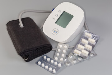 Electronic automatic sphygmomanometer and different medication blisters on gray background