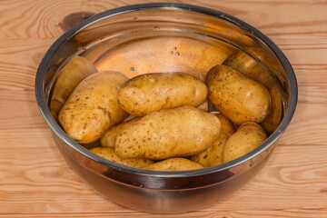 Raw washed yellow potato tubers in stainless steel kitchen bowl