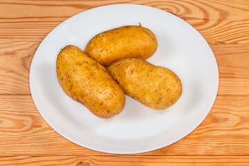 Raw washed yellow potato tubers on plate on rustic table
