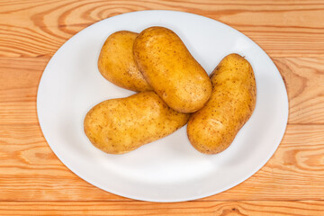 Raw washed yellow potato tubers on plate on rustic table