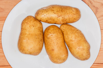 Raw washed yellow potato tubers on white plate close-up