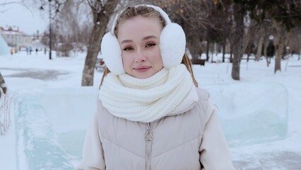 Obraz premium Bundled up in warm winter clothes, a young woman smilingly enjoys the serene snowy landscape, with cozy earmuffs and a stylish scarf providing comfort against the cold