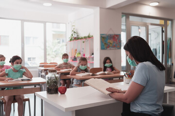 Multiracial group of kids wearing face masks working at class, writing and listening explanations of teacher in classroom