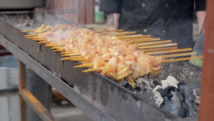 Cooking fires with smoky festival atmosphere, Grilling chicken on skewers amid lively festival heat and smoke, Rows of skewers roasting over embers during animated festival preparations with steady