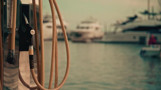 Various hoses coloured in yellow, green, and blue, hang beside modern marina fuel pumps, boat at the fuel station