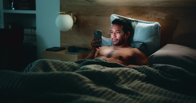 Man, phone and website in bed for temptation, self pleasure and masturbation in home. Night, secret and person with smartphone for pornography, addiction and sneaky activity in bedroom of apartment