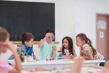 Elementary School Science Classroom: Enthusiastic Teacher Explains Chemistry to Diverse Group of Children, Little Boy Mixes Chemicals in Beakers. Children Learn with Interest