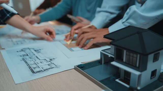 A diverse team of architects collaborates on an innovative construction project reviewing blueprints and a model house in a vibrant office atmosphere, showcasing creativity. SACTR