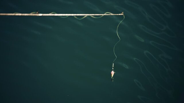 A fishing line and float gently drifting on dark water, minimal and serene