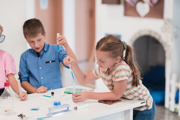 Elementary School Science Classroom: Enthusiastic Teacher Explains Chemistry to Diverse Group of Children, Little Boy Mixes Chemicals in Beakers. Children Learn with Interest