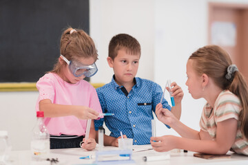 Elementary School Science Classroom: Enthusiastic Teacher Explains Chemistry to Diverse Group of Children, Little Boy Mixes Chemicals in Beakers. Children Learn with Interest