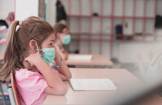 Multiracial group of kids wearing face masks working at class, writing and listening explanations of teacher in classroom - Powered by Adobe