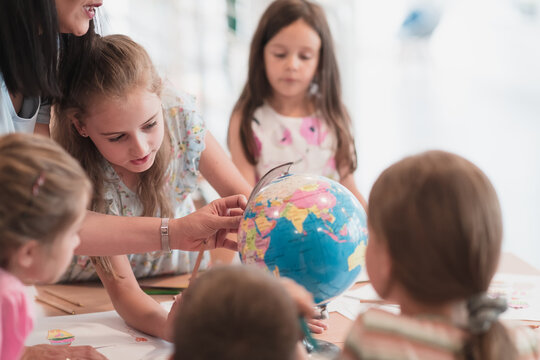 Female teacher with kids in geography class looking at globe. Side view of group of diverse happy school kids with globe in classroom at school.
