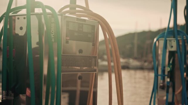 Various hoses coloured in yellow, green, and blue, hang beside modern marina fuel pumps, boat at the fuel station