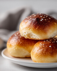 Fototapeta premium A close-up shot of three golden-brown brioche buns sprinkled with coarse salt, stacked on a white plate.