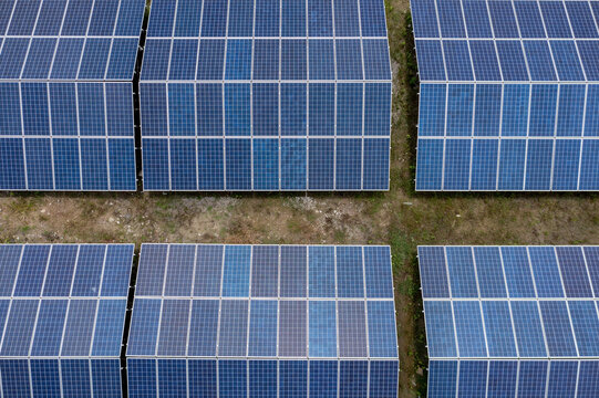 Aerial view of symmetrical solar panels reflecting the sky, creating a geometric blue pattern against the dull ground, Kaptai, Chittagong Division, Bangladesh.