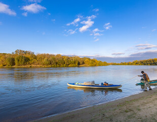 Man is standing on the beach next to a blue kayak