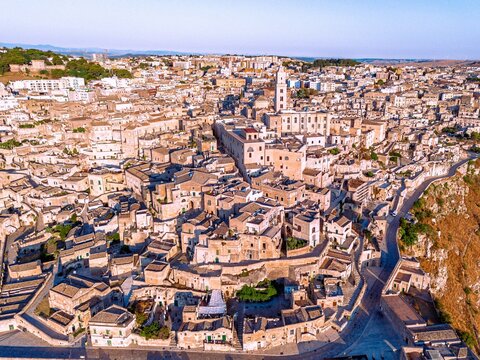 Aerial view of ancient dwellings cascade down the rocky hillside, bathed in warm sunlight, revealing the timeless beauty of the Sassi di Matera, Matera, Basilicata, Italy.