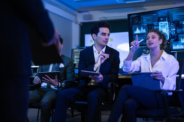Team of diverse financial analysts and IT experts actively discussing an innovative business strategy at command center. Woman raises her hand to contribute a key idea regarding global market trends