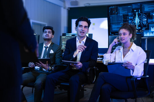 Team of diverse financial analysts and IT experts actively discussing an innovative business strategy at command center. Woman raises her hand to contribute a key idea regarding global market trends - Powered by Adobe