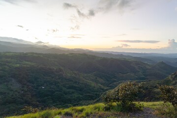 Obraz premium Foreground Grass and Shrubs Framing a Panoramic Sunset over Tropical Hills