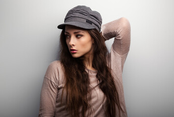 Naklejka premium Sexy makeup brunette female model with long hair posing in elegant sweater and grey fashion cap on light grey studio background with empty space. Closeup style portrait