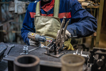 A man at the workshop desk screws nuts with a screwdriver. Atmospheric industrial photography...