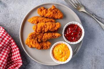 Fried chicken breast strips on grey table background. Delicious chicken crisps