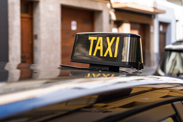 Close-up of an illuminated taxi sign on the roof of a car in an urban street.