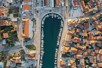 Aerial view of a tranquil harbor cradling a fleet of boats, hemmed by buildings with terracotta roofs, reflecting the warm sunlight, Stari Grad, Split-Dalmatia County, Croatia.