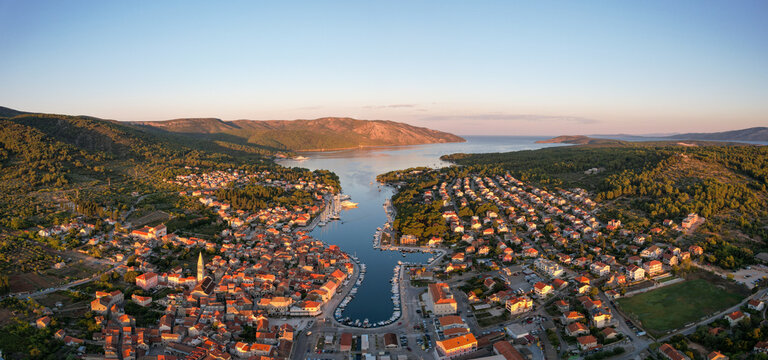 Aerial view of terracotta rooftops cascade down to meet the azure harbor, nestled between verdant hills and the shimmering sea, Stari Grad, Split-Dalmatia County, Croatia.