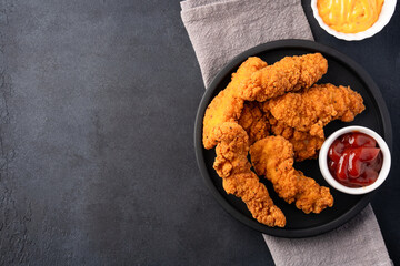 Fried chicken breast strips on black table background. Delicious chicken crisps	
