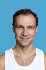 Fototapeta premium Portrait of Caucasian middle aged man smiling and looking into camera against blue background, showing natural facial expression and wearing sleeveless shirt